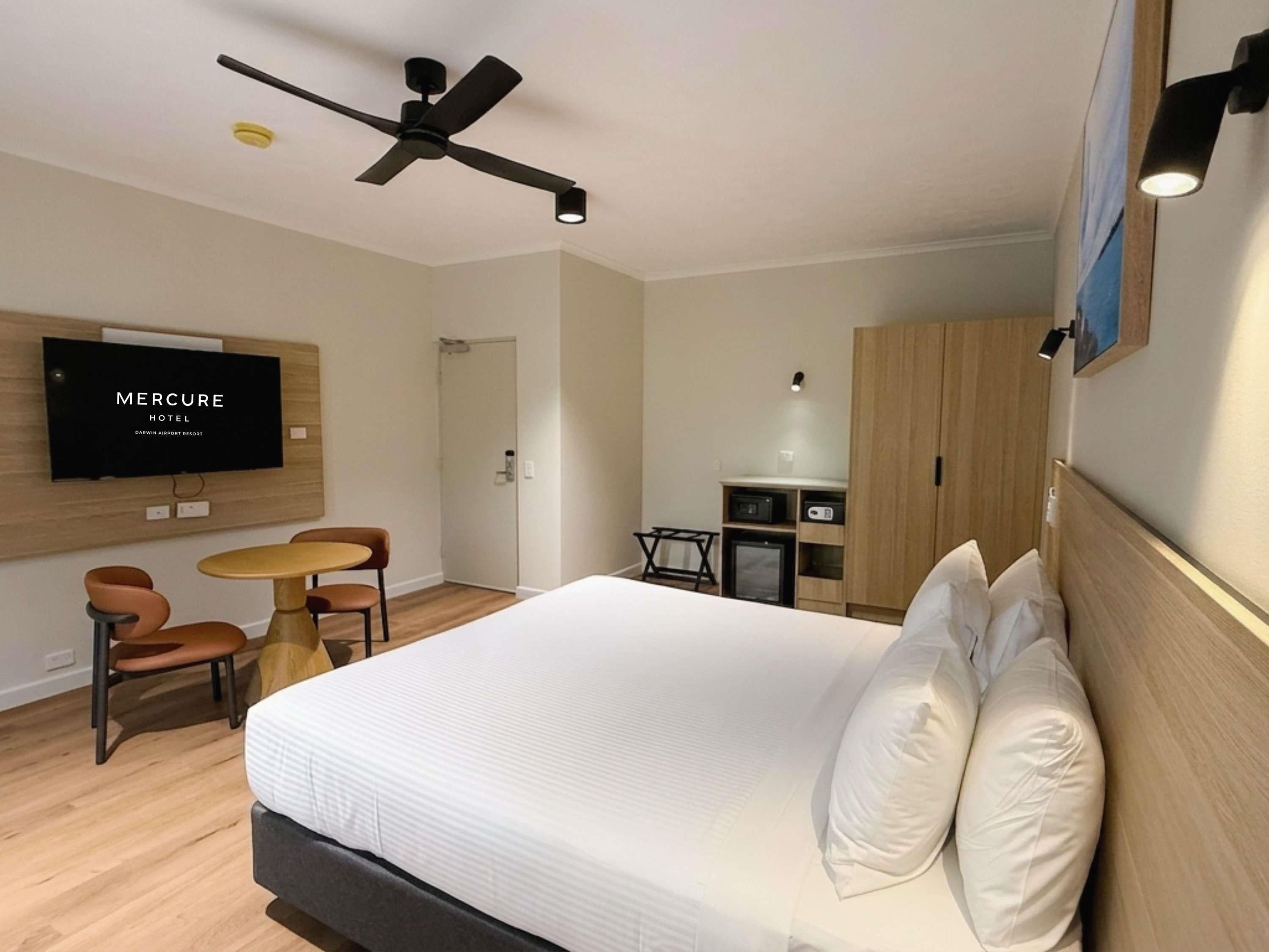 A hotel room with a bed, a desk, a chair, a television, and a ceiling fan.