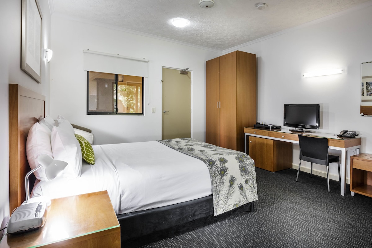 A hotel room with a bed, desk, chair, TV, and a bathroom door.