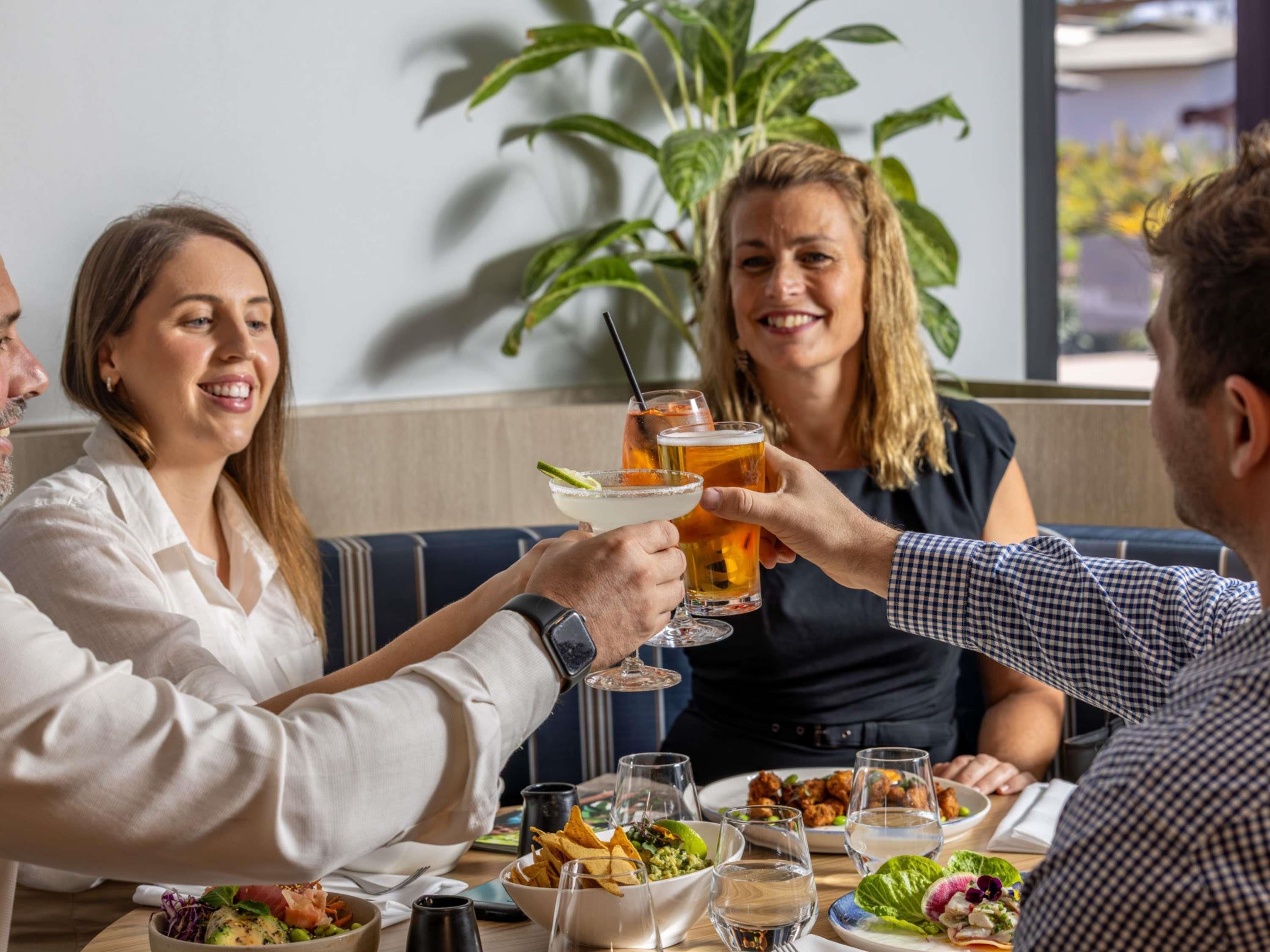 En gruppe mennesker skåler med drikkevarer ved et bord med forskellige retter og glas.