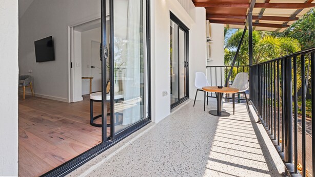 A modern balcony with glass doors, a wooden floor, and a table with chairs. - Mercure Darwin Airport Resort (Eaton)