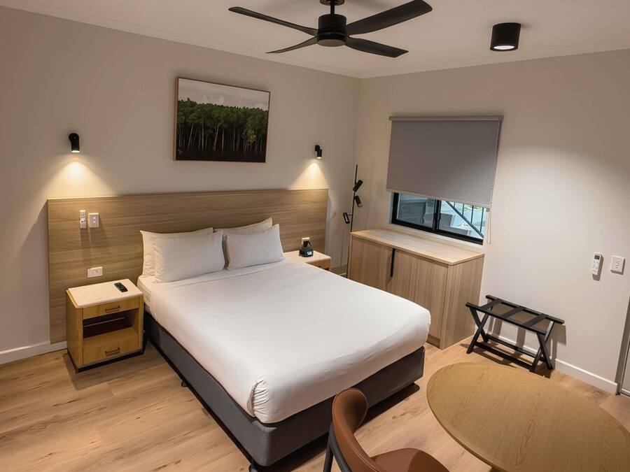 A modern bedroom with a bed, bedside table, nightstand, and a desk with a chair.