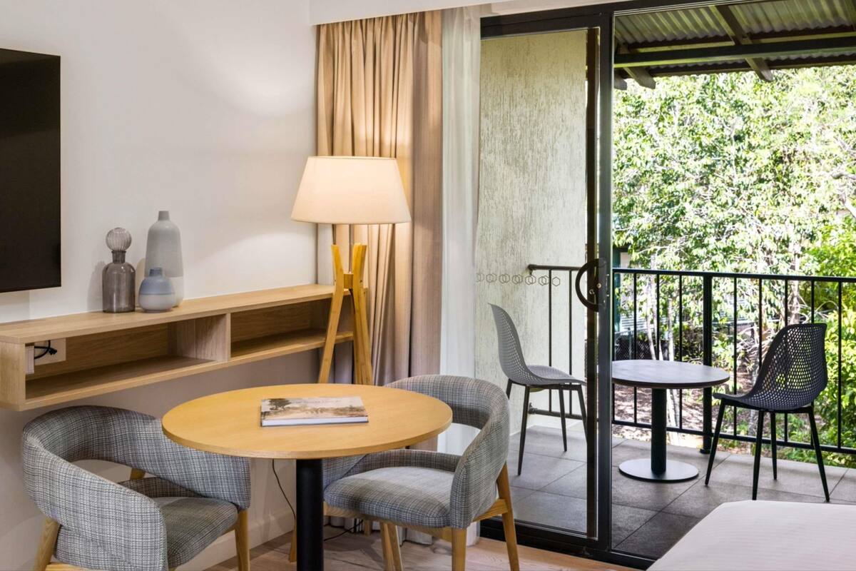 Quarto de hotel com varanda, sofá, mesa e televisão.