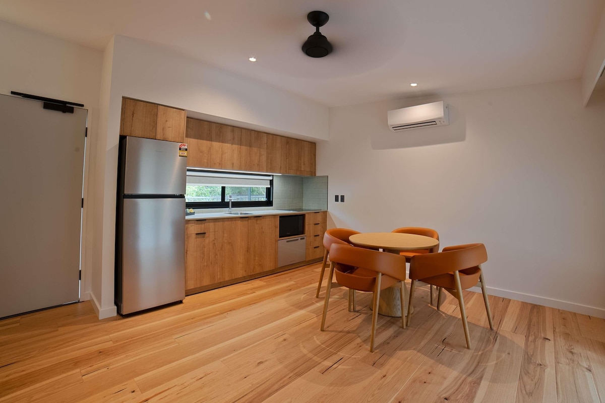 Una cocina moderna con armarios de madera, un refrigerador de acero inoxidable y una mesa de comedor redonda con sillas naranjas.