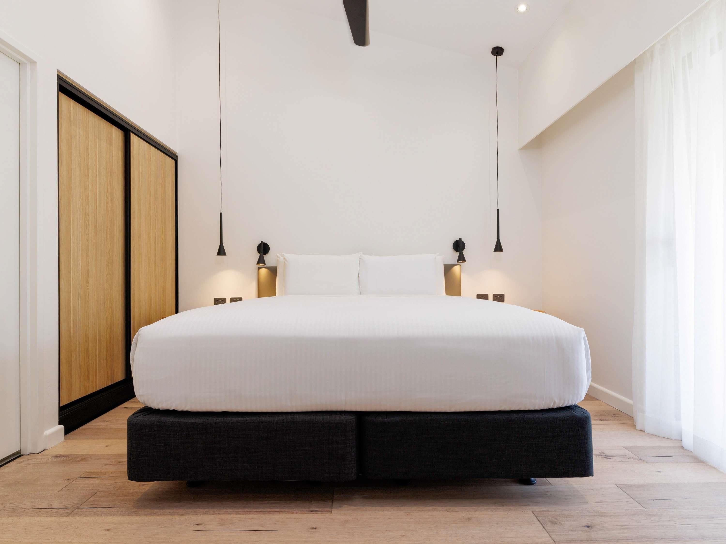 A modern bedroom with a large bed, two bedside tables with lamps, a wooden wardrobe, and a ceiling fan.