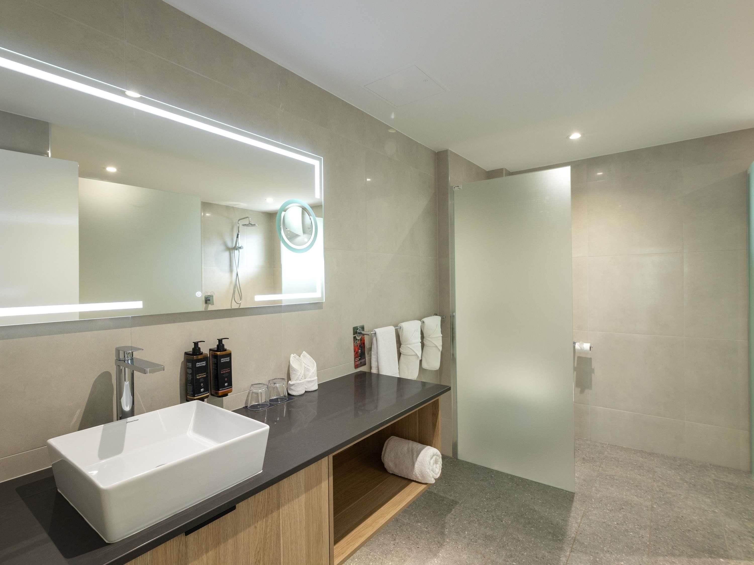 A modern bathroom with a large mirror, a white sink, and a shower area.