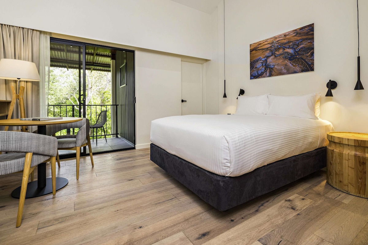 Un dormitorio con cama, un escritorio y una silla, un cuadro en la pared y un balcón.