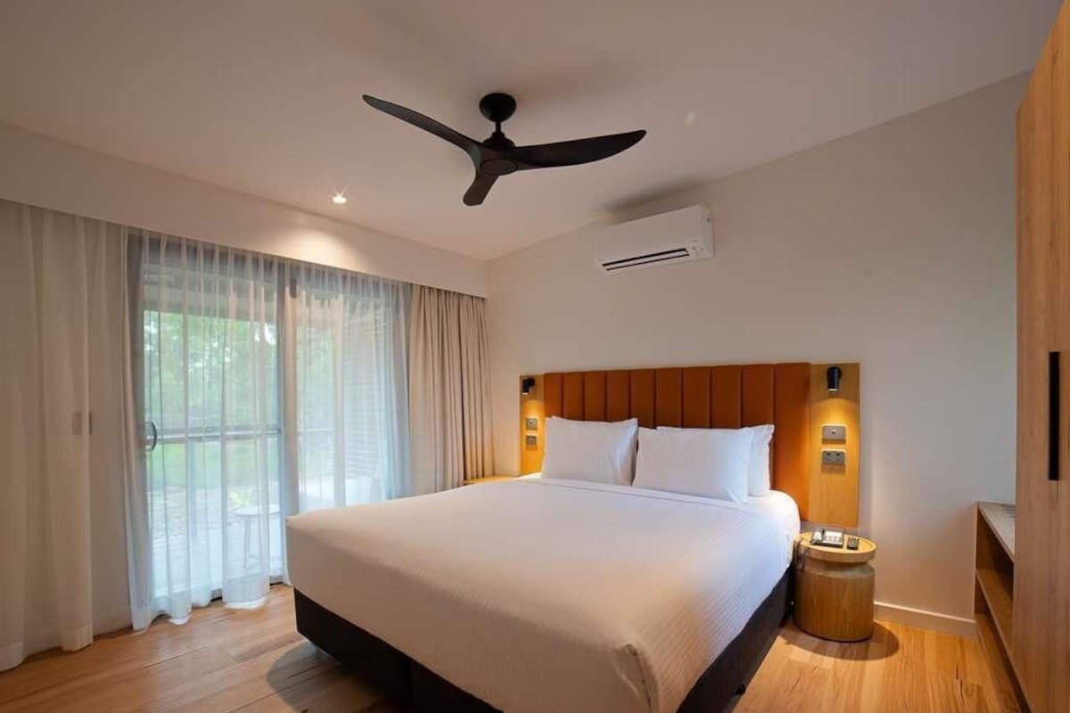 A hotel room with a large bed, a ceiling fan, an air conditioning unit, and a wooden headboard.