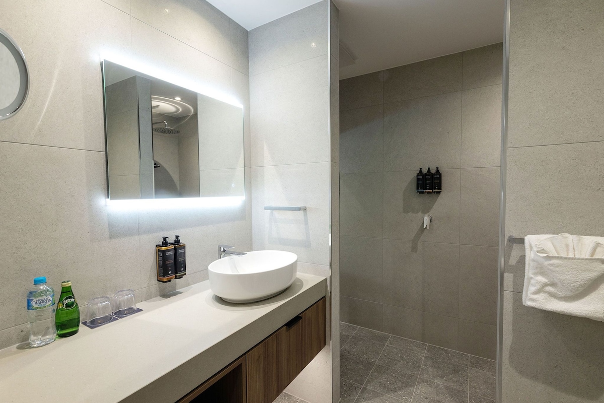 A modern bathroom with a large mirror, a round sink, and a glass-enclosed shower.