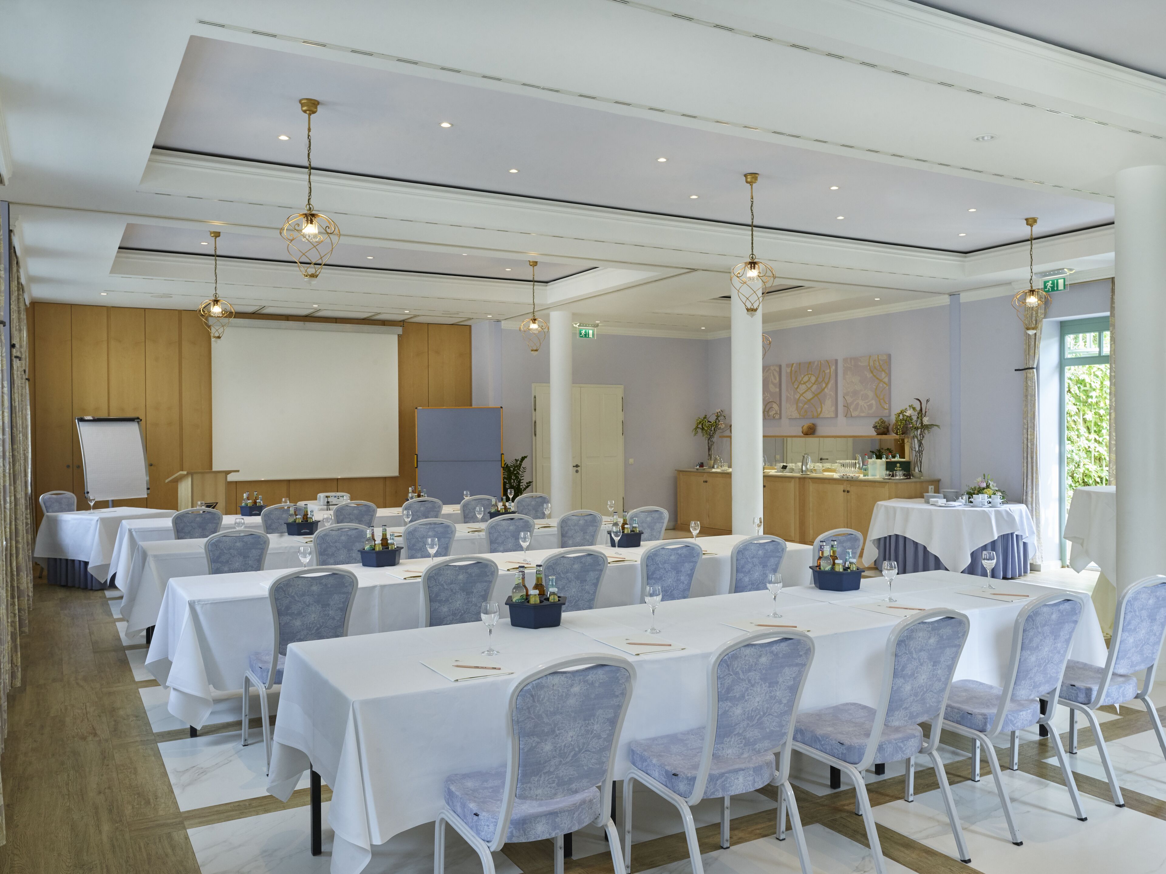 A conference room with multiple tables, chairs, a projector screen, and a podium.