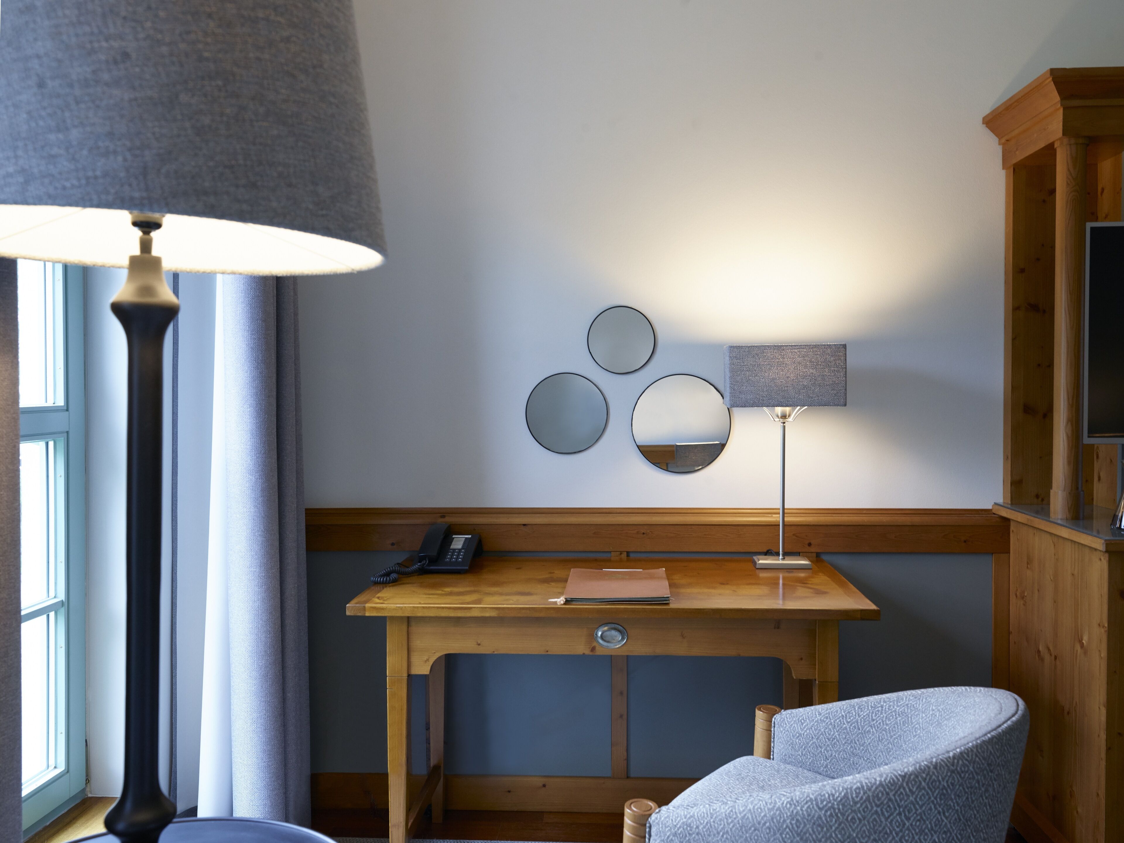 A room with a wooden desk, a chair, a lamp, a telephone, and a television.