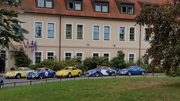 A row of classic cars parked in front of a building with a red-tiled roof and multiple windows.