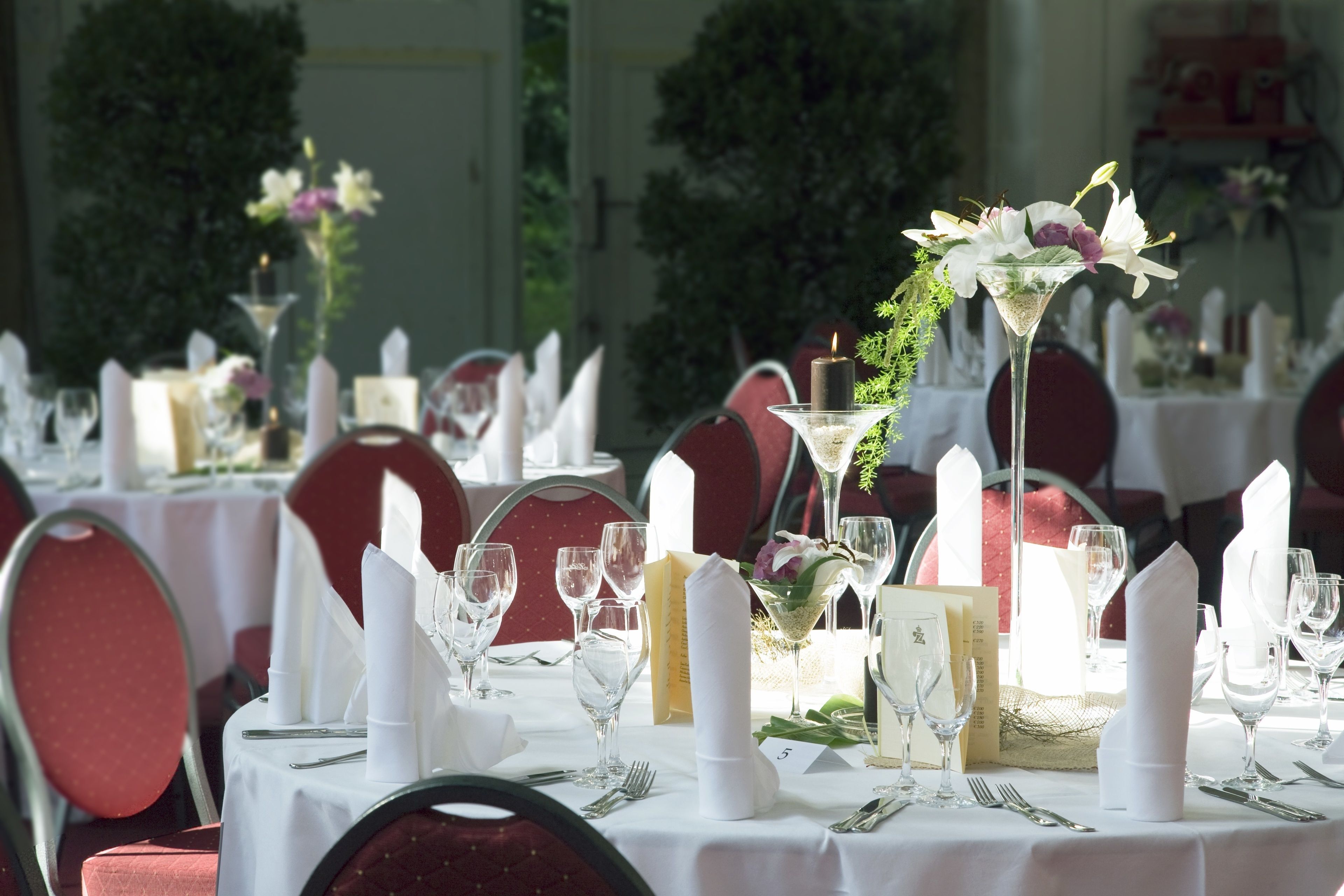 Ein Tisch ist für ein festliches Essen gedeckt, mit weißen Tischdecken, roten Stühlen und floralen Mittelpunkten.