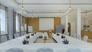 Een vergaderzaal met lange tafels, stoelen en een scherm voor een beamer.