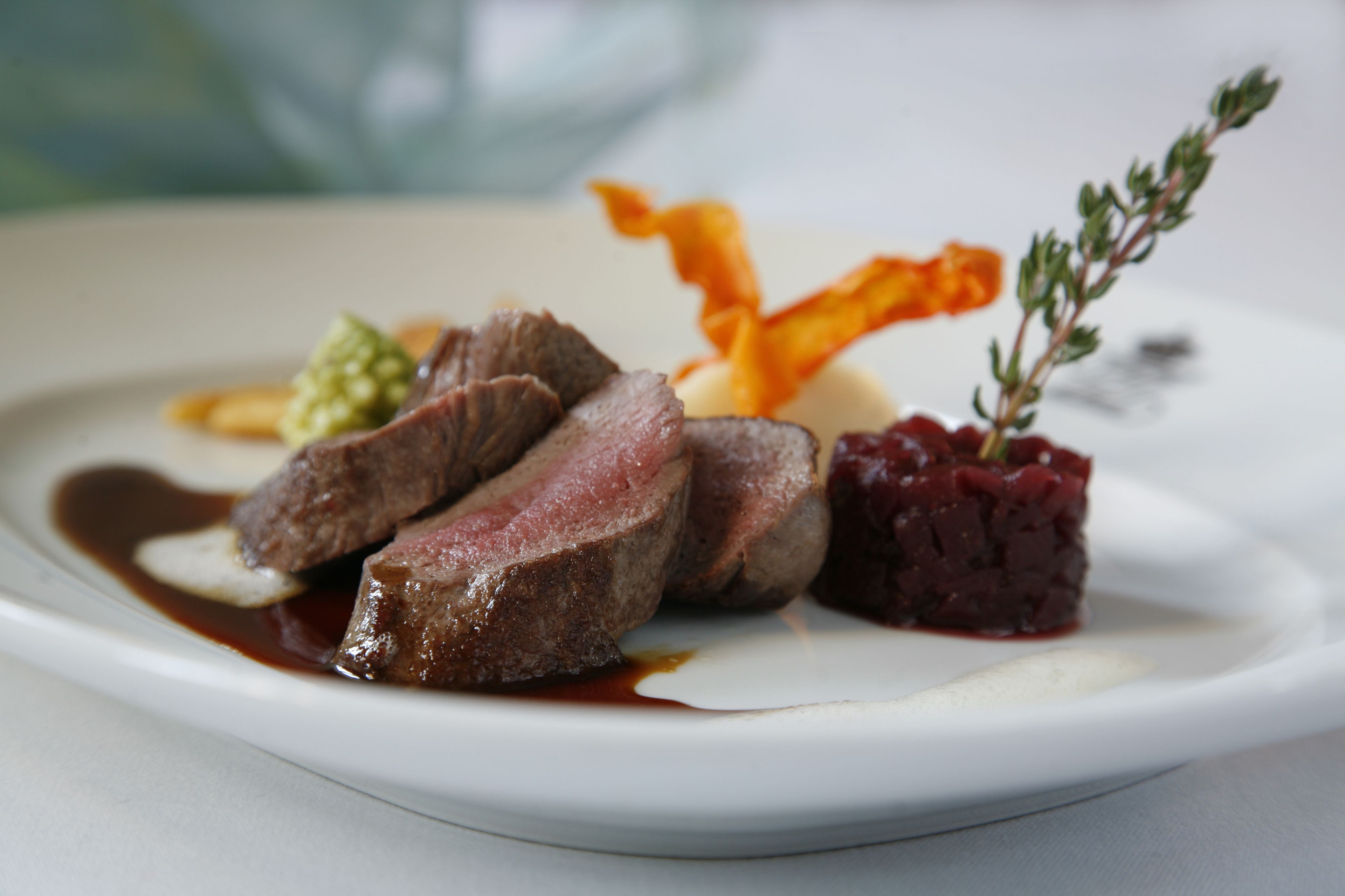 Un piatto con carne a fette, un purè rosso e una guarnizione.