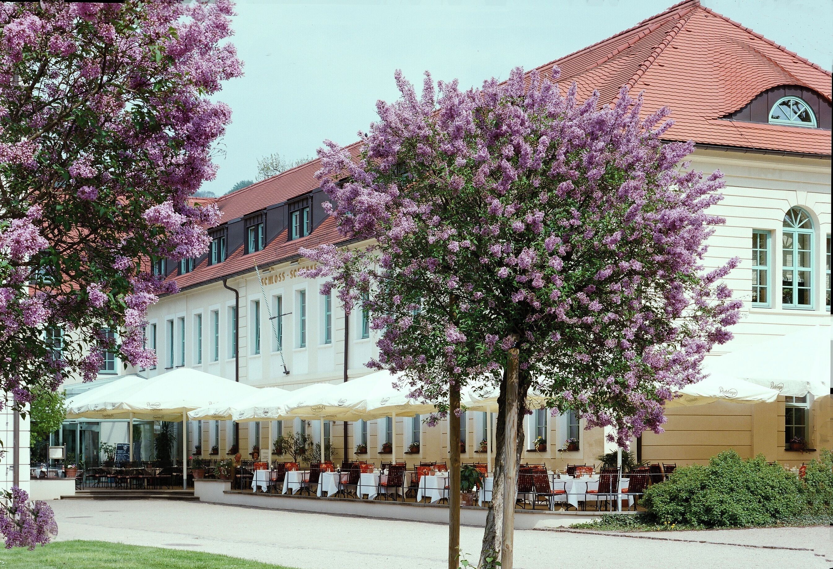 A building with a red roof and white facade, featuring outdoor seating with white umbrellas.