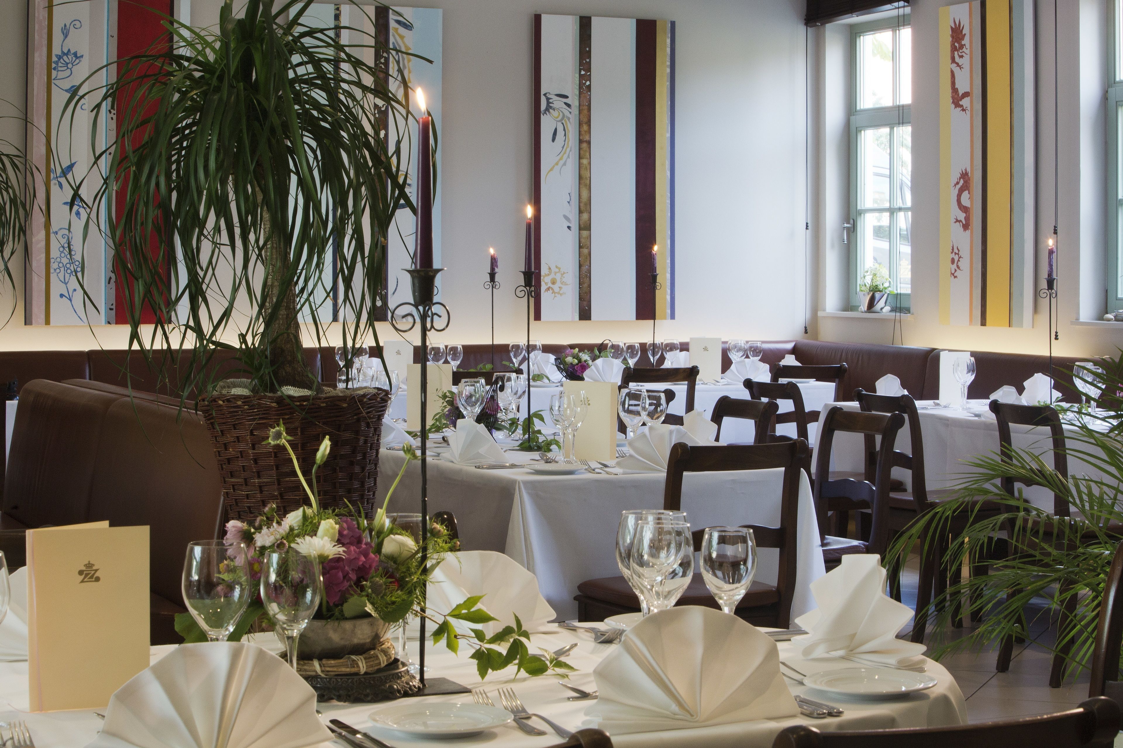 Interior de restaurante con mesas dispuestas para comer, decoración en la pared y plantas en macetas.