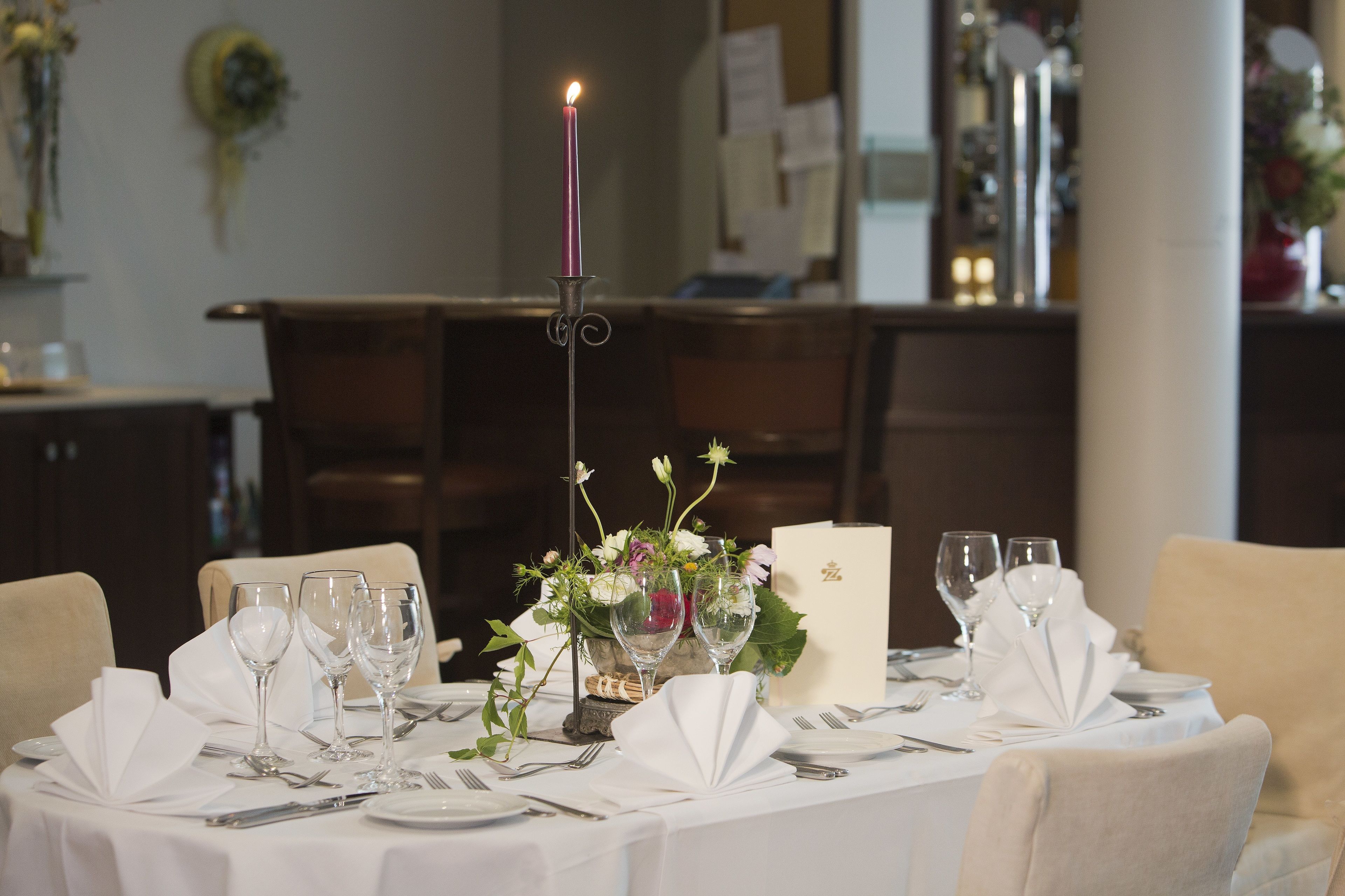 Une table à manger dressée pour un repas, avec une nappe blanche, de la verrerie et un chandelier en guise de centre de table.