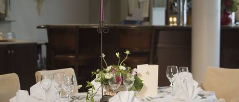 A dining table set for a meal with white tablecloth, glassware, and a candle centerpiece.