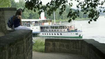 Un ferry con cabinas y asientos en la cubierta, atracado en un muelle de piedra. Una persona está sentada en el borde.