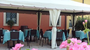 Un espace extérieur aménagé avec des tables et des chaises, protégé par un auvent blanc et entouré de fleurs roses.