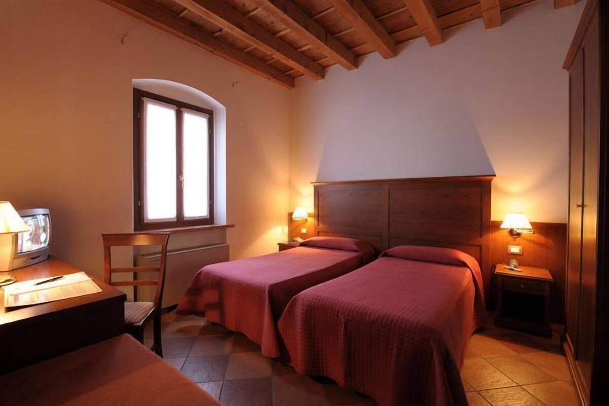 Une chambre avec deux lits, un bureau en bois avec une lampe, une chaise et une fenêtre.
