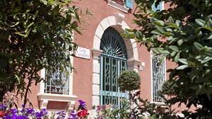 Une façade d’immeuble avec une enseigne indiquant « Corte Castello », une grille en fer forgé et un petit arbre devant.