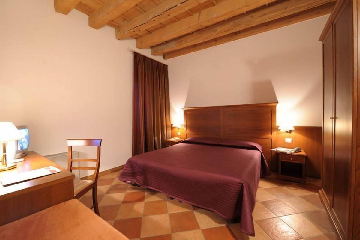 Une chambre d’hôtel avec un plafond en bois, un lit recouvert d’une courtepointe violette, un bureau en bois avec une lampe, une chaise et un téléviseur.