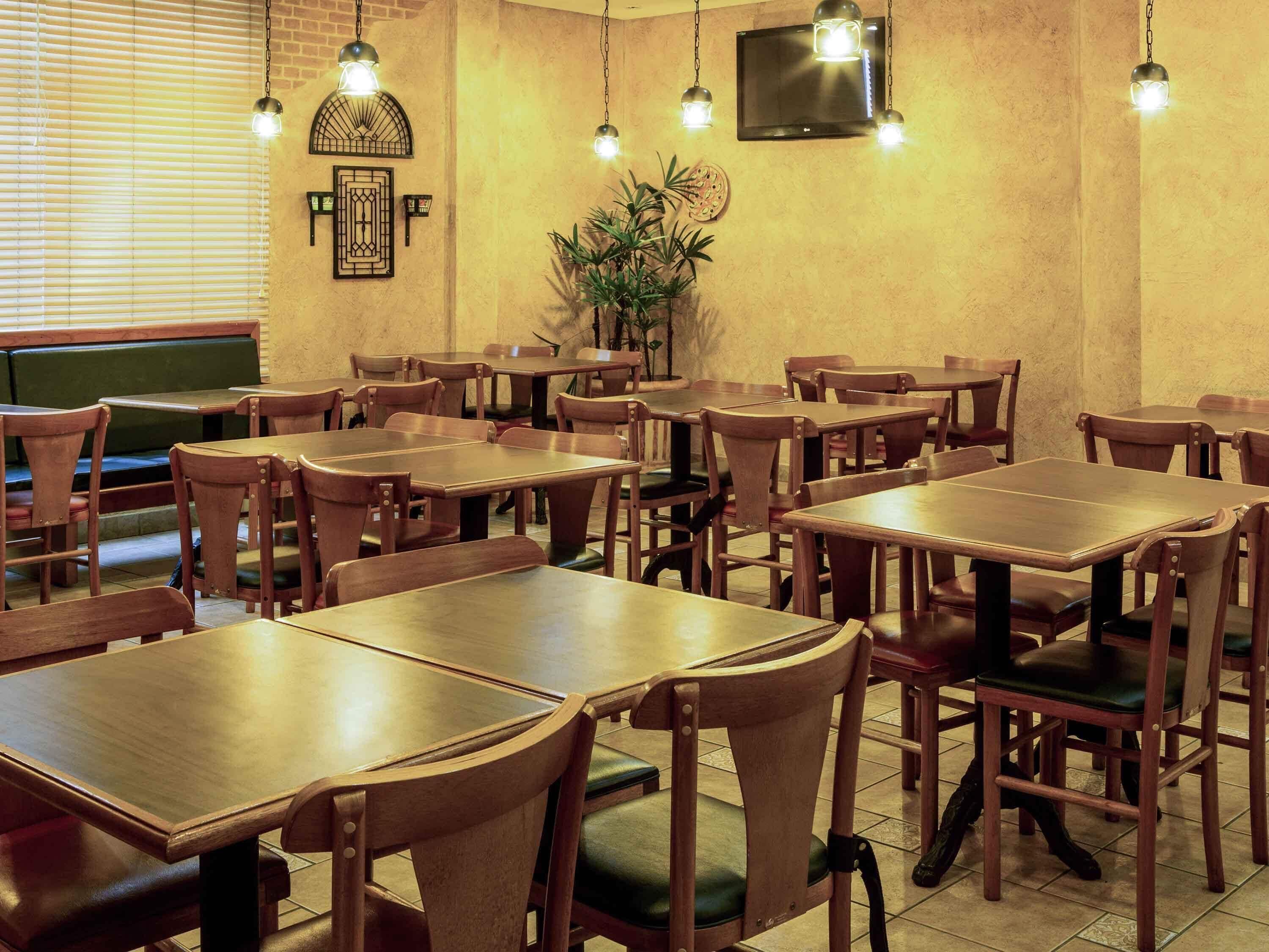 Un interior de restaurante con mesas y sillas de madera, lámparas colgantes, un televisor de pantalla plana y una planta en maceta.