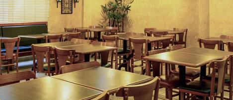 Un interior de restaurante con mesas y sillas de madera, lámparas colgantes, un televisor de pantalla plana y una planta en maceta.