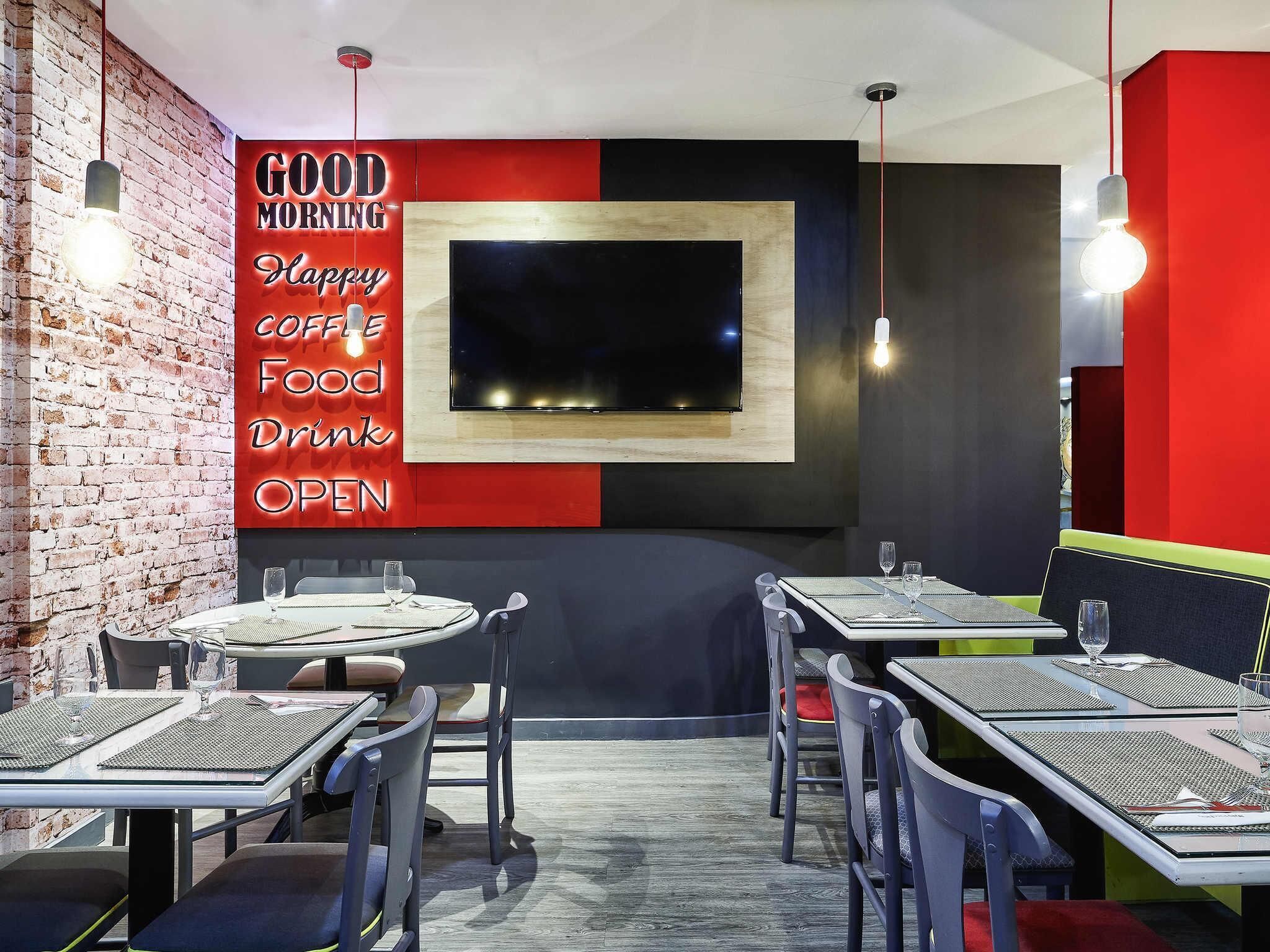 L'intérieur d'un café moderne, avec des murs en briques, une décoration rouge et noire, et de nombreuses tables accompagnées de chaises.