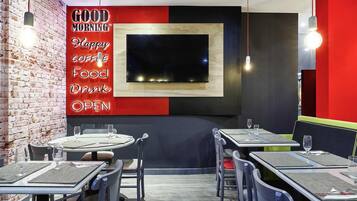 L'intérieur d'un café moderne, avec des murs en briques, une décoration rouge et noire, et de nombreuses tables accompagnées de chaises.