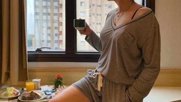 A person standing by a window with a city view, holding a cup. - ibis Taubate (Taubate)