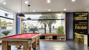 A billiards room with wooden tables, a large window with a view of palm trees and buildings, and a sign with motivational text. - ibis Taubate (Taubate)