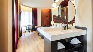 Una habitación de hotel moderna con una cama grande, un espejo redondo, un escritorio y una silla.