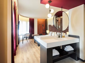 A modern hotel room with a large bed, a round mirror, a desk, and a chair. - ibis Styles Madrid Maravillas (Madrid)