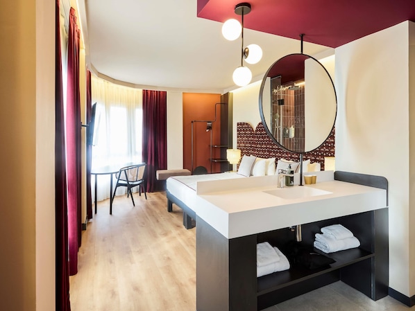 A modern hotel room with a large bed, a round mirror, a desk, and a chair. - ibis Styles Madrid Maravillas (Madrid)