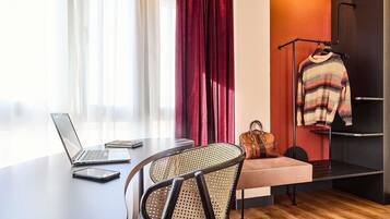 A modern room with a laptop on a desk, a chair, a sofa, a hanging bag, and a wardrobe.