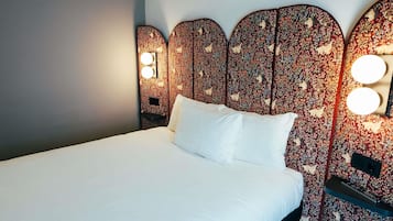 A bed with white linens, a headboard with a floral pattern, and two wall-mounted lights.
