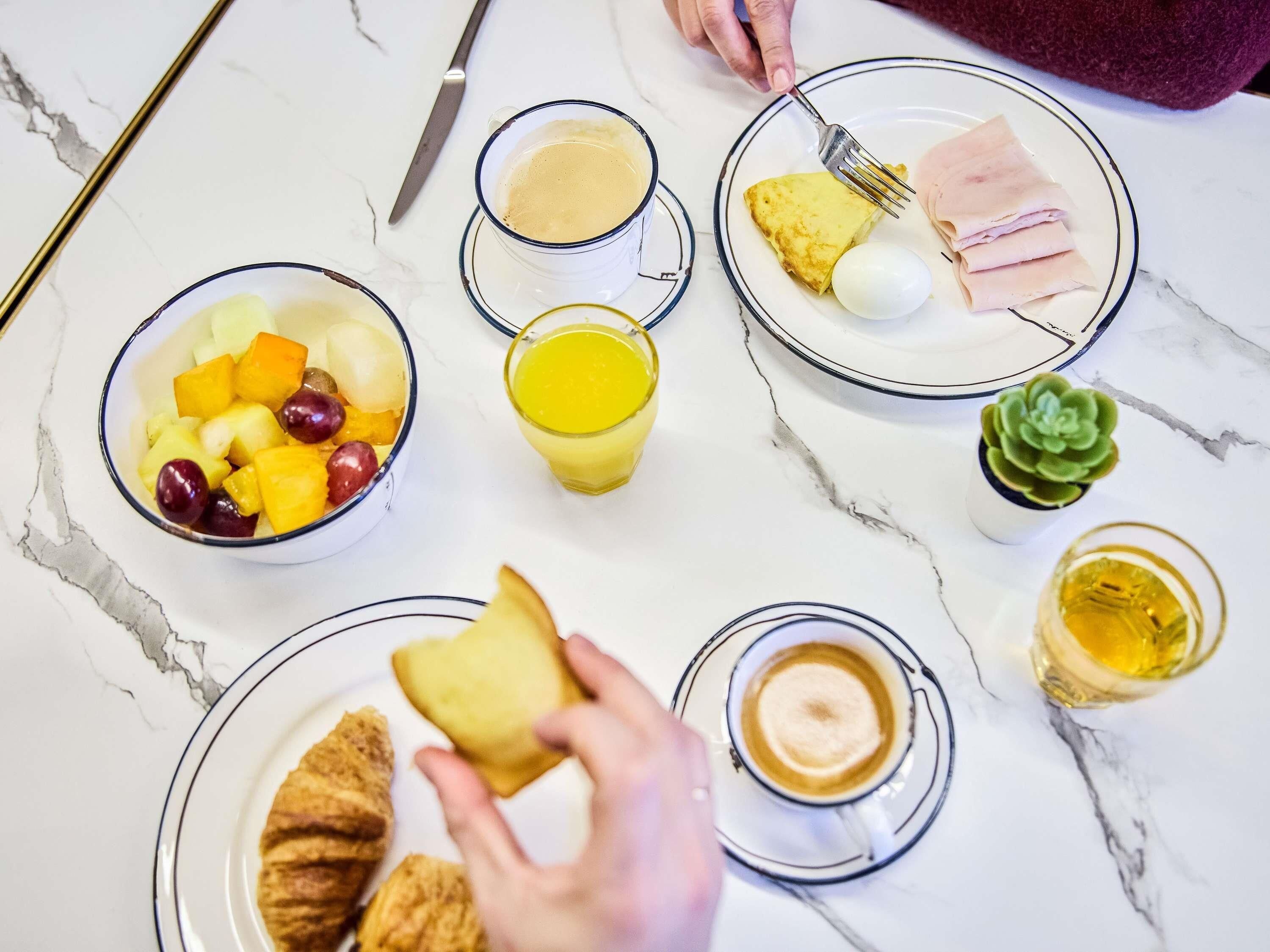 A breakfast setting with a bowl of fruit, a glass of orange juice, a plate with eggs and ham, a cup of coffee, and a croissant.