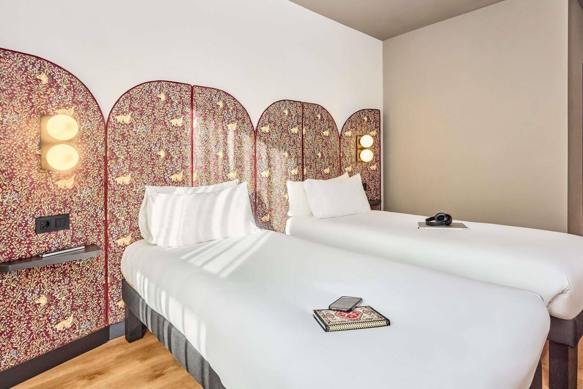 A hotel room with two beds, a decorative headboard, bedside lamps, and a bedside table with a phone and book.