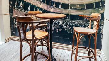 A theater with wooden chairs and tables, a wooden floor, and a balcony with a crowd.
