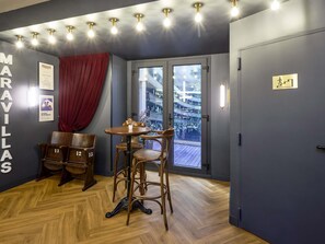 Una habitación con piso de madera, una mesa con sillas, una cortina roja y una puerta con un cartel.