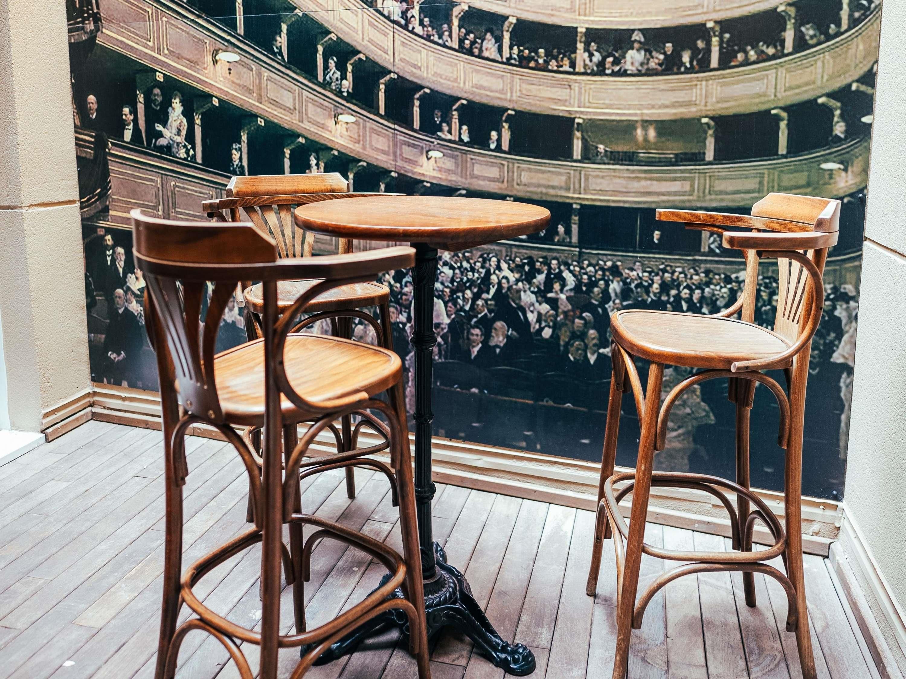 Un théâtre avec des chaises et des tables en bois, un plancher en bois et un balcon où se tient une foule.