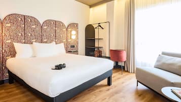 Une chambre d’hôtel avec un lit, un canapé, un fauteuil rouge, un porte-manteau suspendu et un miroir.