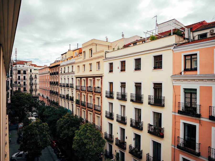 Una hilera de edificios de varios pisos con balcones, una calle debajo y árboles en primer plano.