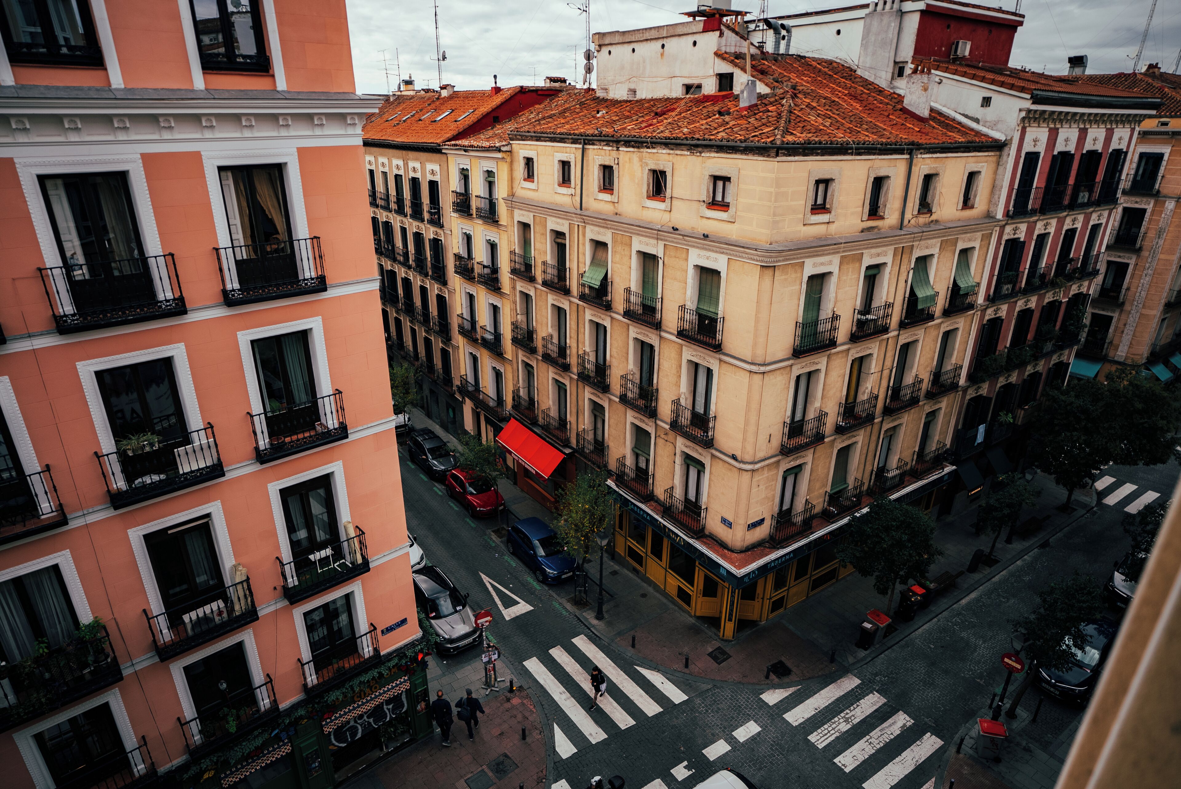 Un edifici d'alguns pisos amb balcons, un pas de zebra i cotxes aparcats.
