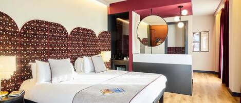 A modern hotel room with a large bed, a bedside table, a mirror, and a view of the hallway.