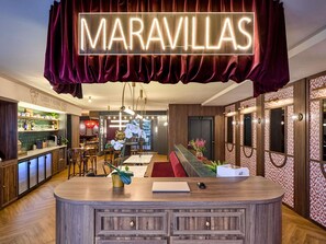 A bar area with a neon sign, wooden furniture, and a view of the city. - ibis Styles Madrid Maravillas (Madrid)