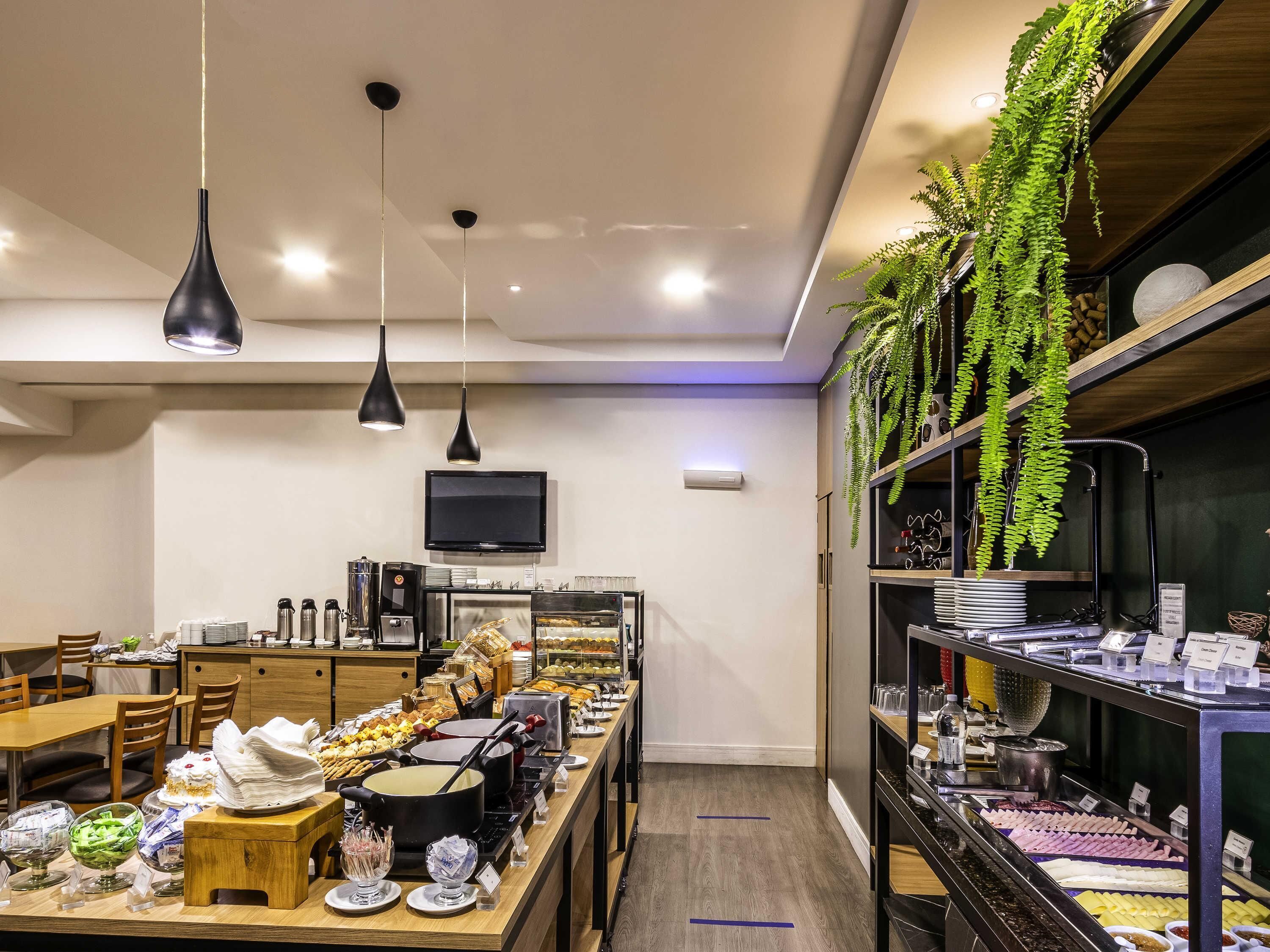 Un restaurante con barra de ensaladas, mesas de madera, plantas colgantes y un televisor en la pared.