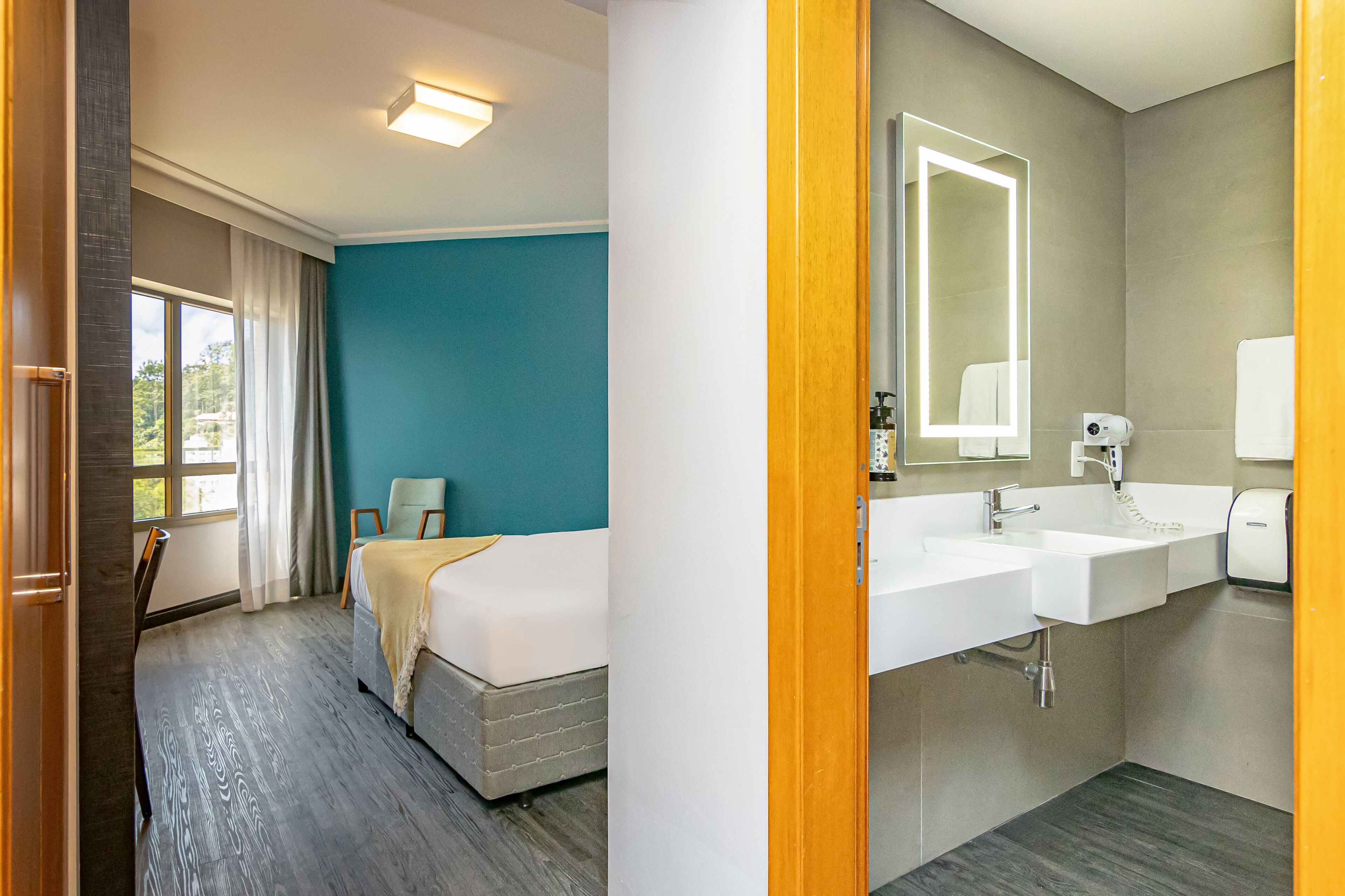 Una habitación de hotel con una cama, una silla, un espejo grande, un lavabo y una ventana con cortinas.